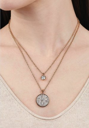 Dos collares de cadena de oro con colgantes redondos de piedras preciosas claras, uno más pequeño y alto, el otro más grande y bajo, usados en un cuello de piel clara.