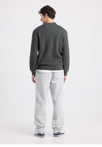 Harmaa ribbineulottu neule pyöreällä kaula-aukolla, yhdistetty vaaleanharmaiden collegehousujen kanssa. Asussa on rento leikkaus ja pehmeä tuntuma.