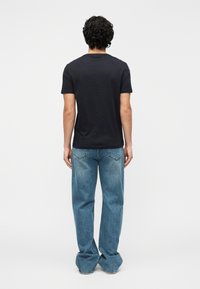 Μαύρο μπλουζάκι με κοντά μανίκια, στρογγυλή λαιμόκοψη και εφαρμοστή γραμμή, συνδυασμένο με ανοιχτό μπλε τζιν παντελόνι με φαρδιά μπατζάκια και ελαφρώς ξεθωριασμένη υφή.