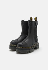 Black ankle boots with a chunky platform, smooth leather upper, elastic side panels, and distinctive yellow stitching. Accented pull tabs.