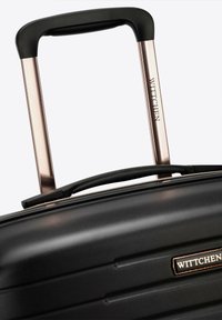 Czarna twarda walizka z pionowymi rowkami, wyposażona w wyściełaną czarną rączkę i wysuwany uchwyt w kolorze różowego złota, oznaczona marką "Wittchen".