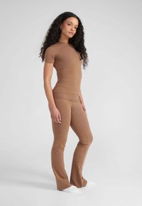 Strak bruin topje in combinatie met bijpassende flared broek, gemaakt van een soepele, rekbare stof. Eenvoudig ontwerp met minimale naden en strakke lijnen.