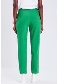 Pantalon vert sur mesure avec une texture lisse, une coupe fuselée et un design minimaliste, doté d'une taille mi-haute et d'ourlets retroussés.