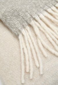Sciarpa in cashmere con una sfumatura di grigio chiaro a crema, con dettagli di frangia morbida su un bordo e una texture liscia.