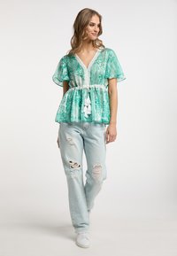 Blusa verde a fantasia con maniche corte a campana e vita con cordoncino. Abbinata a jeans azzurri chiari sbiaditi e strappati e sneakers bianche.