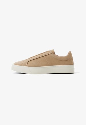 Beige suède instapsneaker met witte rubberen zool, zijstiksel detail en minimalistisch ontwerp, weergegeven vanaf de linkerkant op een witte achtergrond.