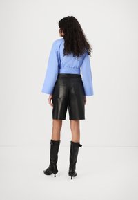 Chemise à manches longues bleu clair avec des poignets larges, associée à un short en cuir noir taille haute et des bottes à talons noires montantes.