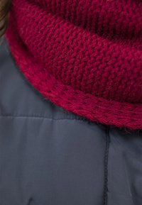 Scarf in magenta con texture a maglia sovrapposto a una giacca imbottita blu scuro, con dettagli a coste e intrecciati nel design della sciarpa.