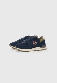 Navy blue sneakers with a suede and mesh upper, featuring a round logo patch, light beige sole, and dark green accents on the collar.