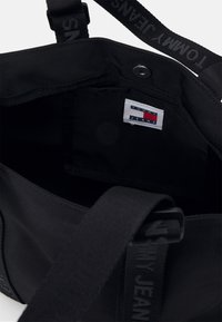 Czarna torba z materiału z metką Tommy Jeans wewnątrz. Projekt obejmuje mocne rączki i kompaktowe, funkcjonalne wnętrze.