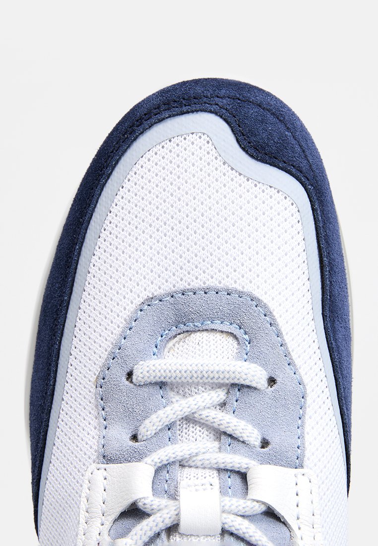 Weißer Mesh-Sneaker mit navyblauen Wildlederakzenten, runder Zehenpartie, hellblauen Schnürsenkeln und einem strukturierten Stoffeinsatz im Zehenbereich. Flache Sohle.