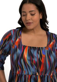 Bunt gemustertes Kleid mit quadratischem Ausschnitt, das fließende Wellenmuster in Blau-, Rot- und Gelbtönen zeigt, aus weichem Stoff gefertigt.