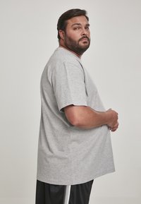 T-shirt gris à manches courtes avec un col rond, à coupe décontractée, fabriqué en tissu mélangé coton. Accompagné de shorts noirs avec des rayures blanches.