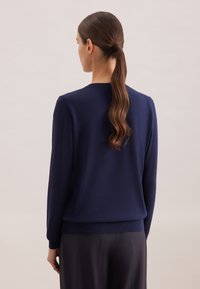 Maglione girocollo blu navy con maniche lunghe, polsini e orlo a costine. Texture morbida, silhouette aderente e dettagli di design minimali.