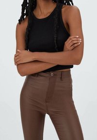 Zwarte geribbelde tanktop gecombineerd met bruin hoge taillebroek. De top heeft een ronde halslijn en de broek heeft voorzakken en een knoopsluiting.