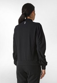 Giacca nera a pullover con colletto alto, polsini a coste e texture arricciata sulle maniche. Tessuto liscio e dettagli minimi.