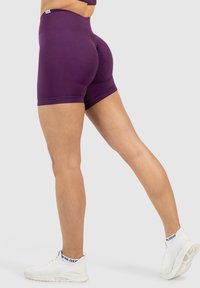 Pantalones cortos deportivos de tiro alto en color púrpura, material elástico, diseño ajustado, textura suave. Combinados con zapatos deportivos blancos.
