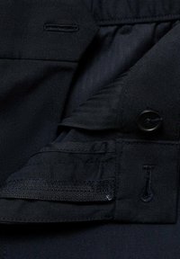 Tissu noir avec une texture lisse, comportant un bouton, des détails cousus et un rabat interne avec fermeture Velcro.