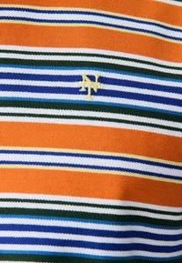 Oranža adīta auduma ar horizontālām svītrām baltā, zilā, zaļā un dzeltenā krāsā, ar nelielu izšūtu krēmkrāsas "N" un "T" monogrammu.