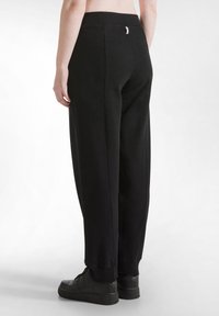 Schwarze, locker sitzende Sweatpants aus weichem Material, mit einem elastischen Bund und gerippten Bündchen. Die Ansicht zeigt Details von hinten und die Schuhe.