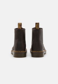 Bottes de cheville en cuir marron avec des coutures jaunes, des poignées en boucle et une semelle en caoutchouc épaisse. Texture lisse sans motifs visibles.