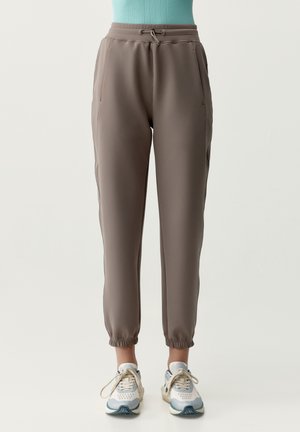 Sivé športové nohavice s orezaným strihom, elastickými manžetami na konci, bočnými vreckami a sťahovacím pásom, nosené s bielymi a modrými teniskami.