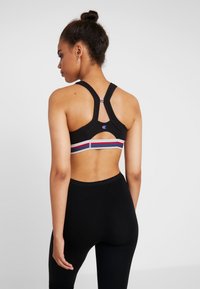Sujetador deportivo negro con un diseño de espalda cortada, presenta franjas horizontales coloridas y un detalle del logo. Combinado con leggings negros.