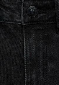 Svart denimtyg med en strukturerad väv, med en silverknapp som har "DENIM LAB" präglat. Närbild av midjebandet och sömnadsdetaljer.