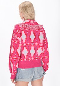 Maglione rosa con motivo geometrico, caratterizzato da frange sul colletto. Abbinato a pantaloni corti di jeans casual.