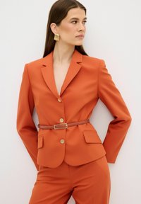 Oranje op maat gemaakte blazer met gouden knopen, slim fit en twee voorkruiken, getailleerd met een bruine riem. Gladde textuur.