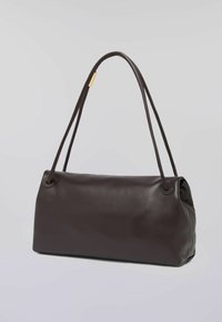 Tmavě hnědá kožená kabelka s měkkou texturou, zaobleným obdélníkovým tvarem, dvěma úzkými ramenními popruhy a minimalistickým designem.