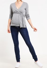 Gray wrap top with a V-neck and side tie, paired with dark blue skinny jeans and white slip-on shoes. Smooth knit texture.