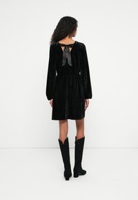 Mustat samettimekko pitkillä hihoilla, takana leikkaus ja nauhavyötärö. Yhdistetty polven korkeisiin mustiin saappaisiin, joissa on terävät kärjet.