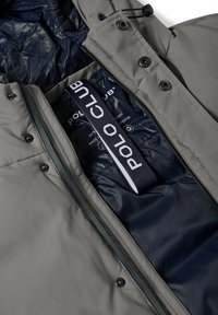 Chaqueta gris resistente a la intemperie con un interior acolchado en azul marino. Las características incluyen botones, un zipper y una etiqueta de marca visible en el interior.