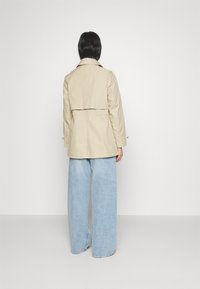 Beige trenchcoat med insvängt midja, knappdetaljer på ärmarna och en klassisk krage, ihop med vida ljusblå jeans.