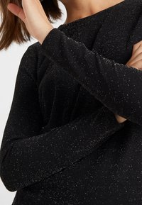 Black long-sleeve top made of soft, textured fabric with metallic gold specks, featuring a boat neckline and fitted sleeves.