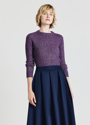 Lila gestrickter Pullover mit Rundhalsausschnitt, kombiniert mit einem marineblauen Faltenrock. Der Pullover hat lange Ärmel und eine strukturierte Oberfläche.