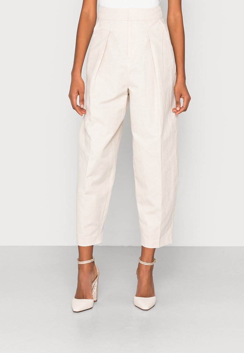 Light beige pleated trousers made of linen, featuring a loose fit and ankle length. Paired with nude block-heel shoes with ankle straps.