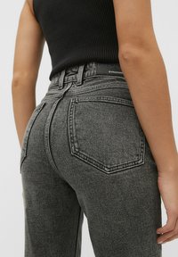 Jeans de mezclilla negros de tiro alto con un lavado desgastado, que cuentan con bolsillos traseros, pasadores para cinturón y una etiqueta en la cintura. Tela texturizada.