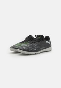 Zapatillas deportivas negras con una parte superior texturizada que presenta patrones lineales en verde y blanco. Cordones negros y una suela de goma gris claro.