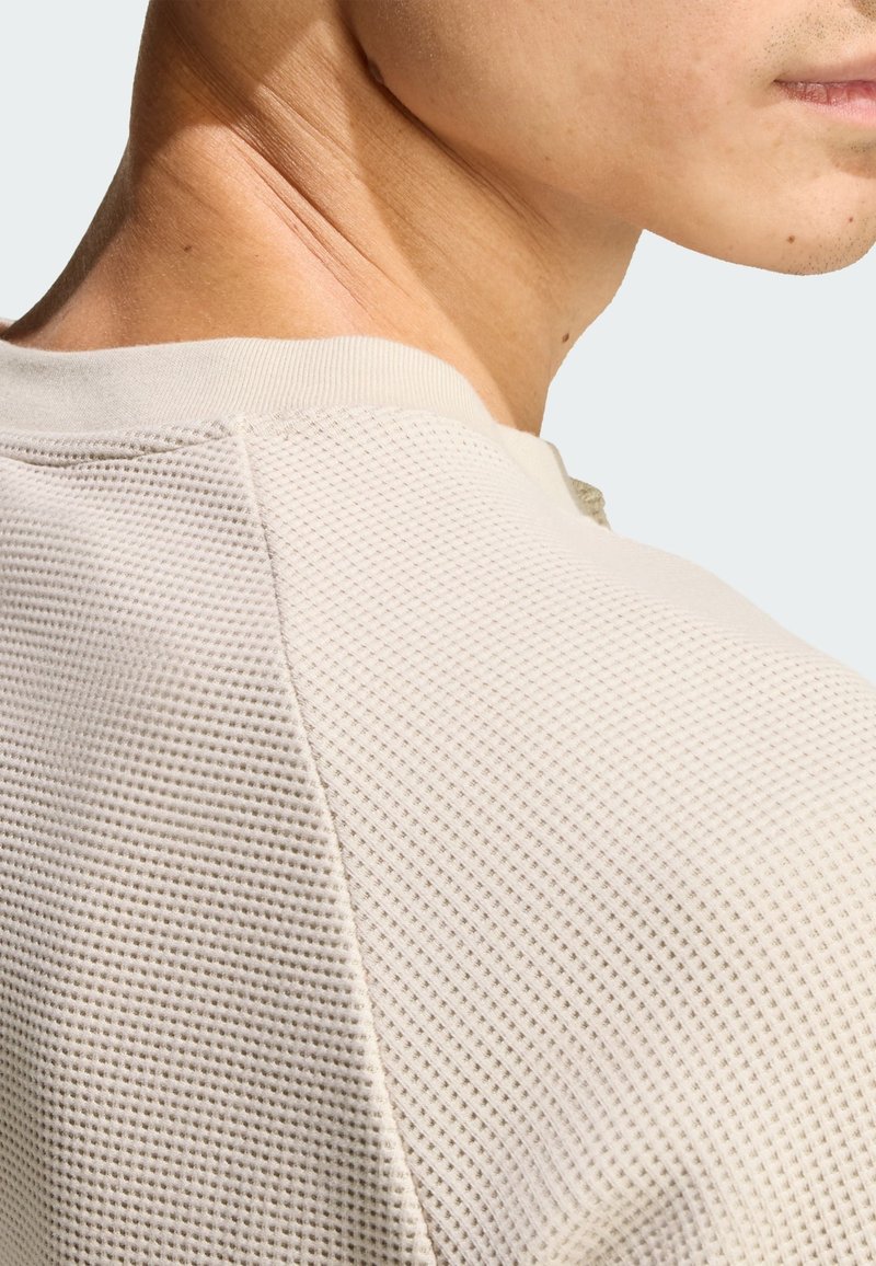 Light beige short-sleeve shirt with a textured, mesh pattern and ribbed neckline. Close-up view of the shoulder and neck area.