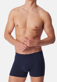 Boxer shorts in cotone blu navy con una vestibilità attillata, caratterizzati da una texture liscia e una cintura elastica, mostrati su un modello maschile a petto nudo.