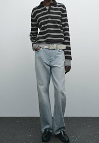 Brown and white striped long-sleeve polo shirt, light blue straight-leg jeans, gray belt, black shoes, standing against a neutral background.