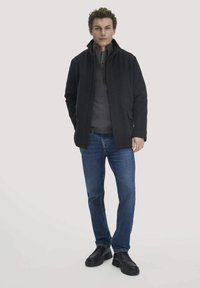 Dunkler Wollmantel für Herren mit hohem Kragen, kombiniert mit einem grauen Fleece-Pullover, blauen Jeans und schwarzen Schnürstiefeln. Glatte Textur und figurbetontes Design.