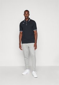 Polo nero con colletto bianco e strisce sulle maniche, caratterizzato da un logo. Abbinato a pantaloni jogger grigi e sneakers bianche. Look semplice e sportivo.