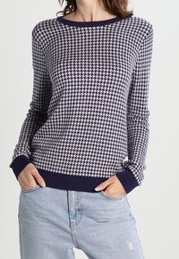 Pull en tricot bleu marine et crème avec un motif à carreaux texturé. Il présente un col rond et des poignets et un ourlet côtelés. Coupe décontractée.