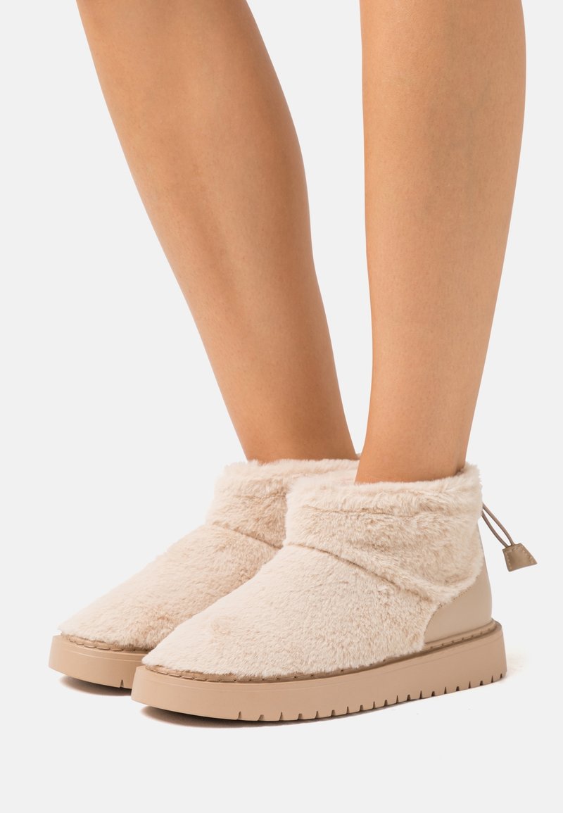 Beige ankle boots featuring a fluffy exterior, smooth leather accents, and a rubber sole with textured patterns. Drawstring detail at the back.