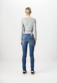 Pull en ribbed gris clair associé à un jean en denim bleu ajusté. Le jean présente un délavage clair et un petit logo sur les poches arrière.