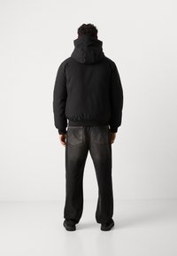 Black hooded jacket with a fitted hem and long sleeves paired with dark, loose-fitting jeans featuring back pockets and a faded finish.