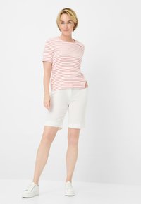 Rot-weiße gestreifte Kurzarmbluse, kombiniert mit knielangen weißen Shorts. Das Modell trägt weiße Sneaker; sauberes, minimalistisches Design.